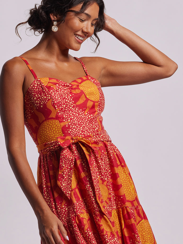 Yellow floral-print sleeveless v-neck sundress, model poses with hand in hair, front view.