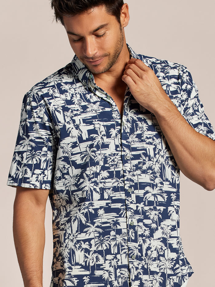 Navy and white tropical-print UPF shirt, man adjusting collar, front view.