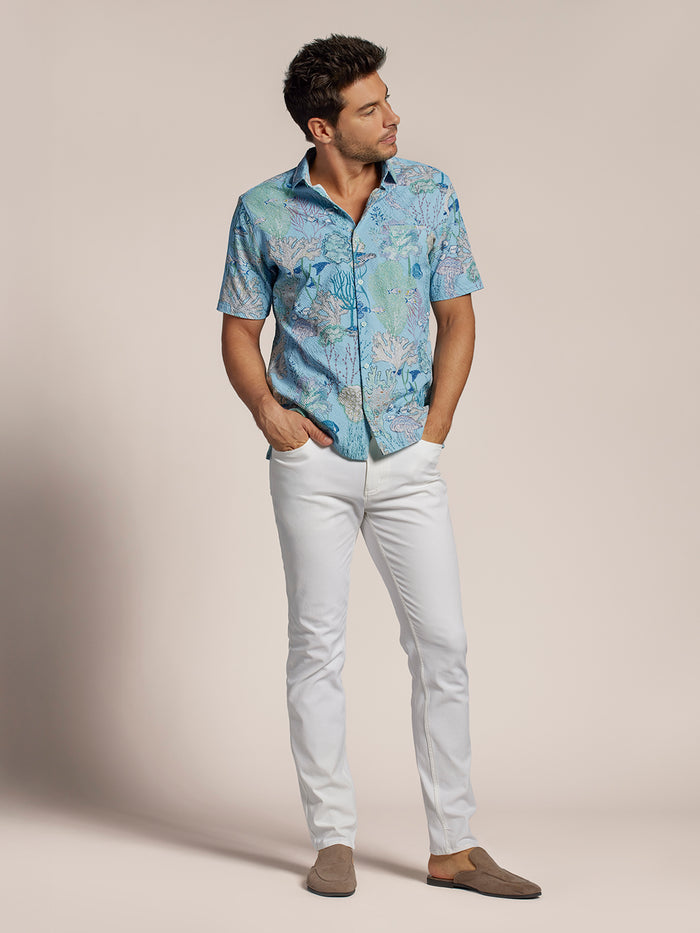 Aquatica coral & fish-print shirt, white pants, brown loafers, front view, hands in pockets.