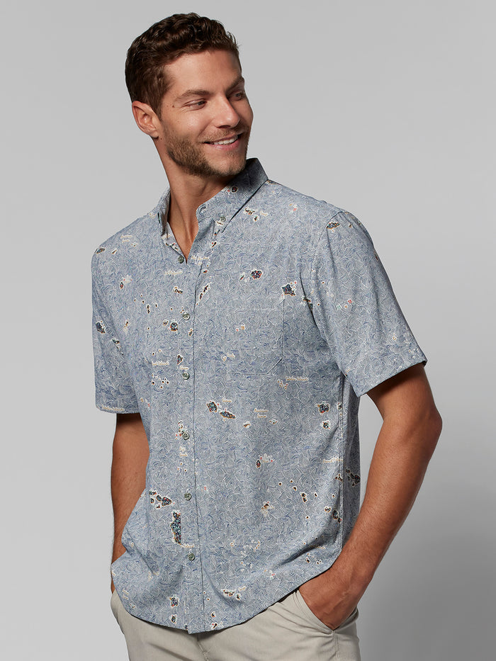 Blue map-print short-sleeve button-up shirt, front view, hands in pockets.