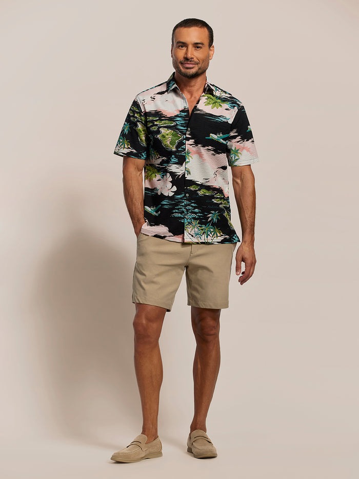 Pink, black, green & blue tropical short-sleeve shirt with island and plane print with khaki shorts, front view of a man.