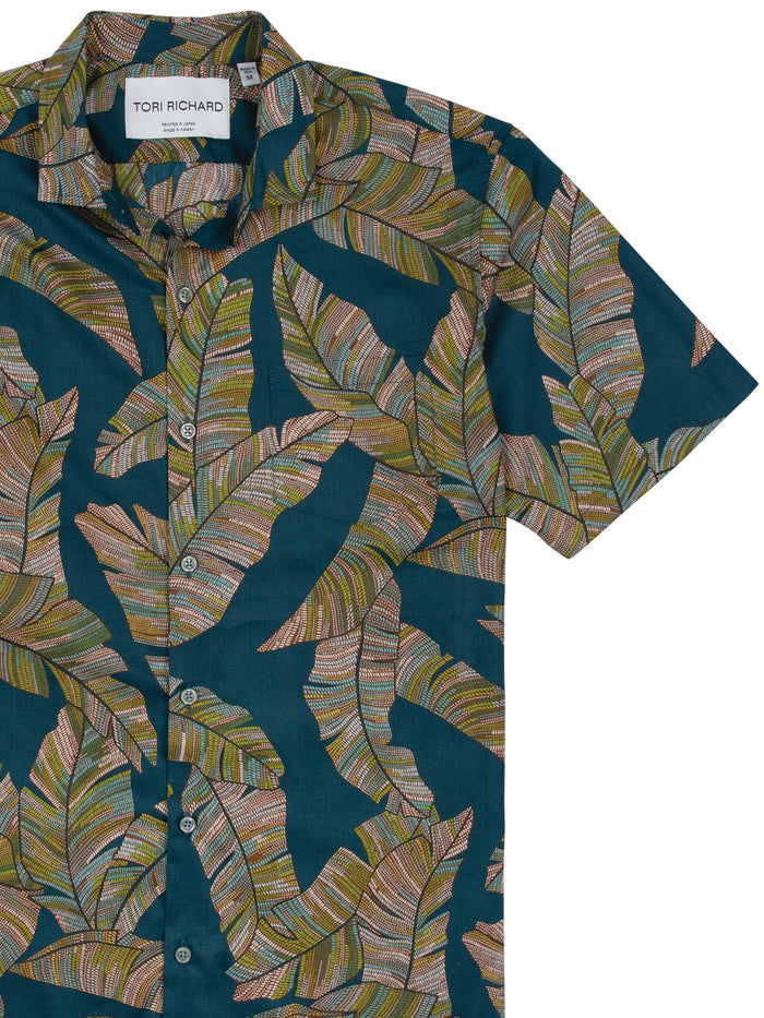 Green and brown leaf print short-sleeve button-up shirt on dark teal cotton lawn, front view.