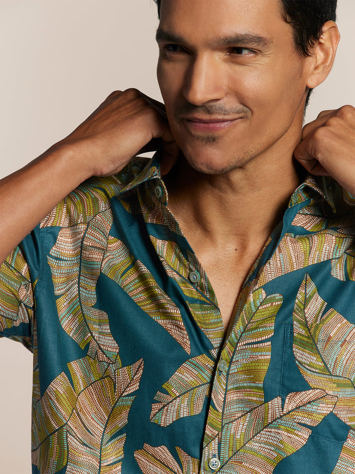 Green and beige leaf-print on teal background short-sleeve shirt, man adjusting collar, front view