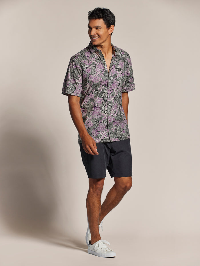 Purple and black floral-print cotton lawn shirt, batik doodle-print cotton shirt with dark shorts and white sneakers, front view .
