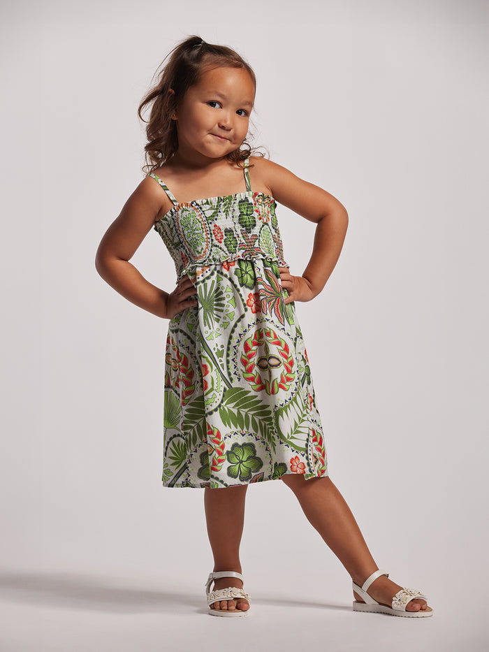 A young girl wearing a sleeveless floral dress with a smocked bodice and flared skirt, standing against a white background.