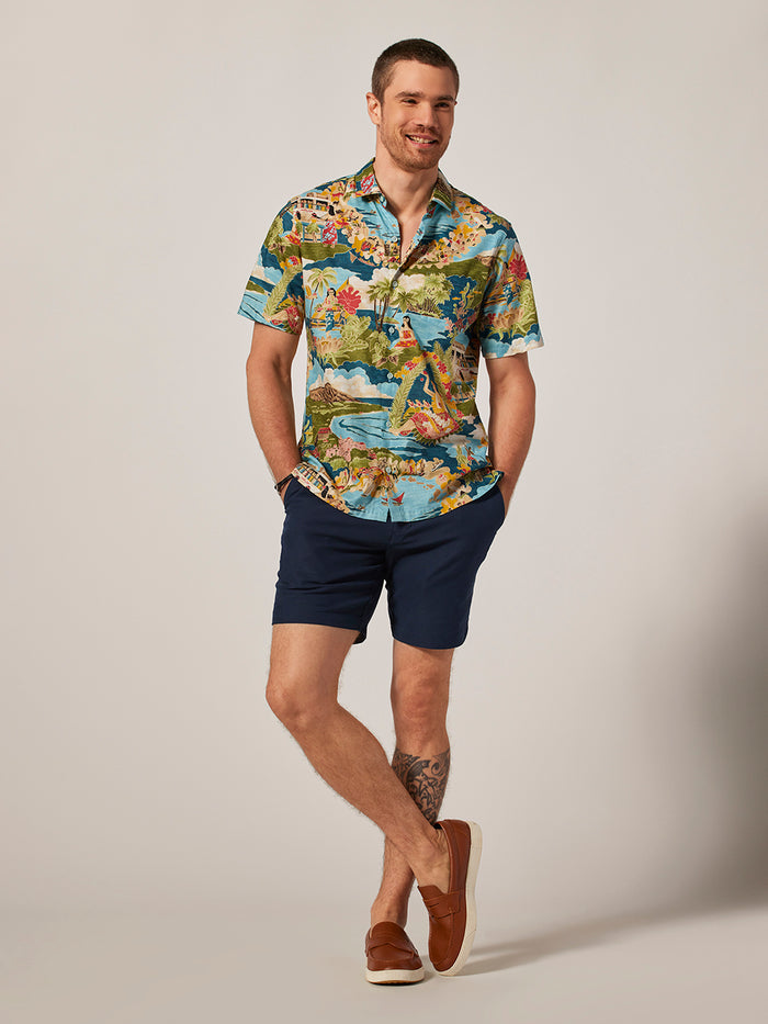 Blue and white floral short-sleeve shirt and navy shorts, front view with crossed leg.