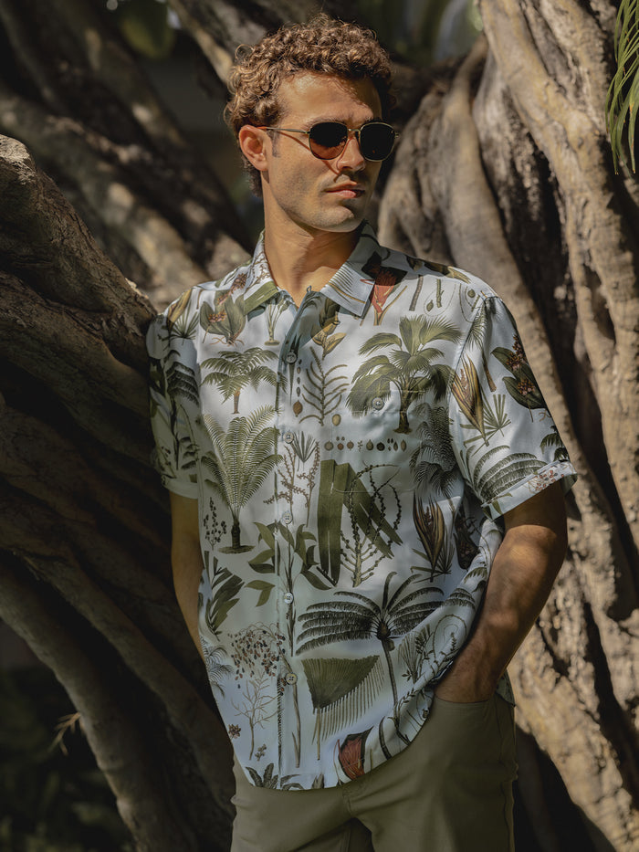 Sky Blue palm-print twill short-sleeve shirt, worn by a model in an outdoor scene near a tree.