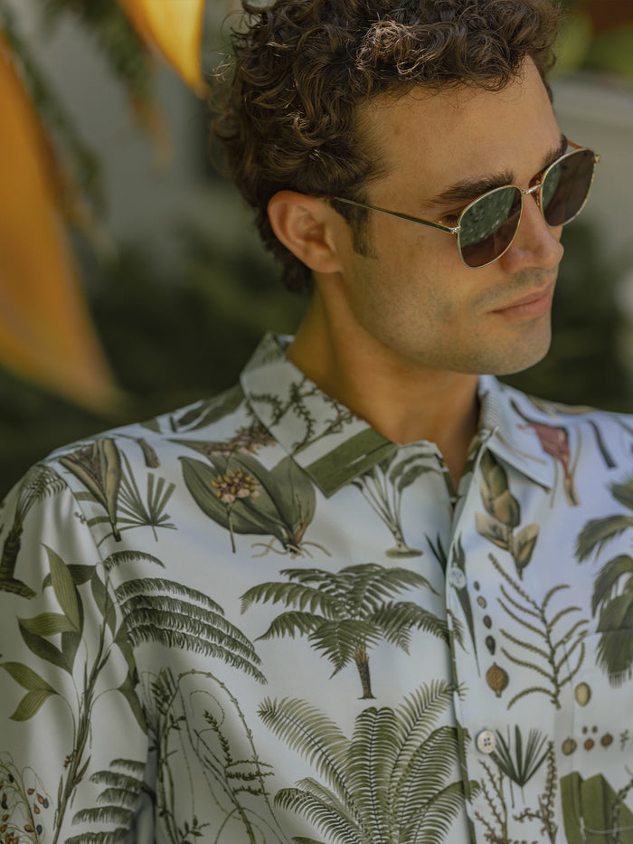Sky Blue palm-print twill short-sleeve button-up shirt, worn by a model with sunglasses, front view.