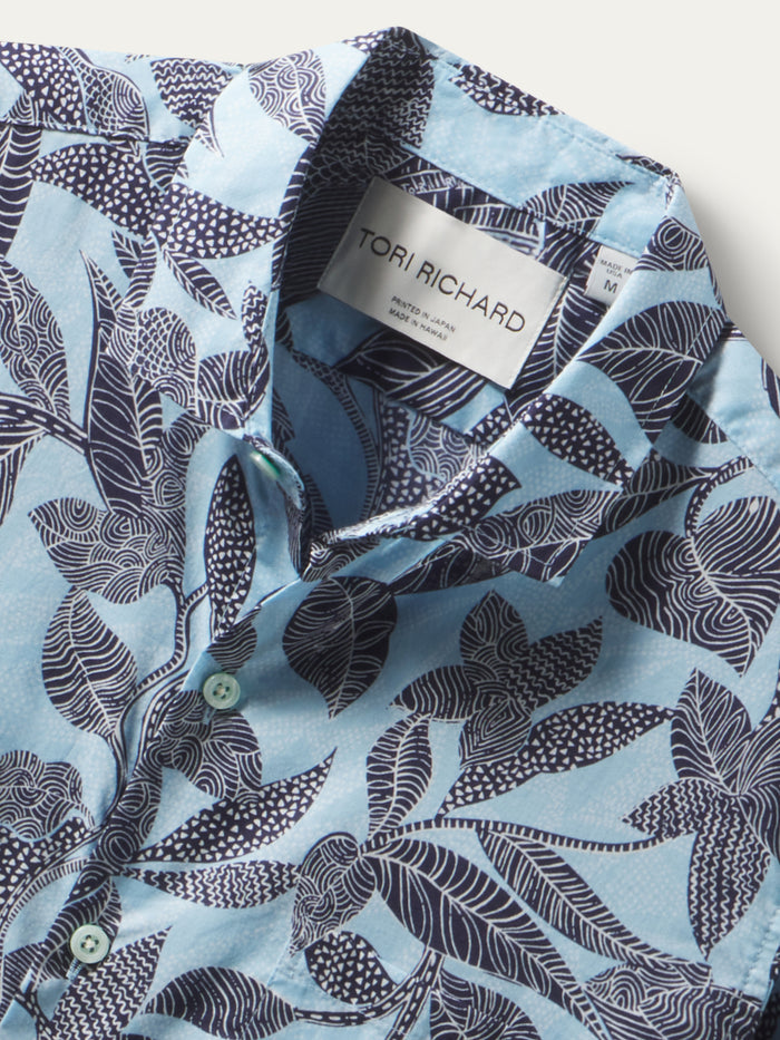 Sky Blue short-sleeve shirt, navy leaf and plumeria print, white buttons, front label.