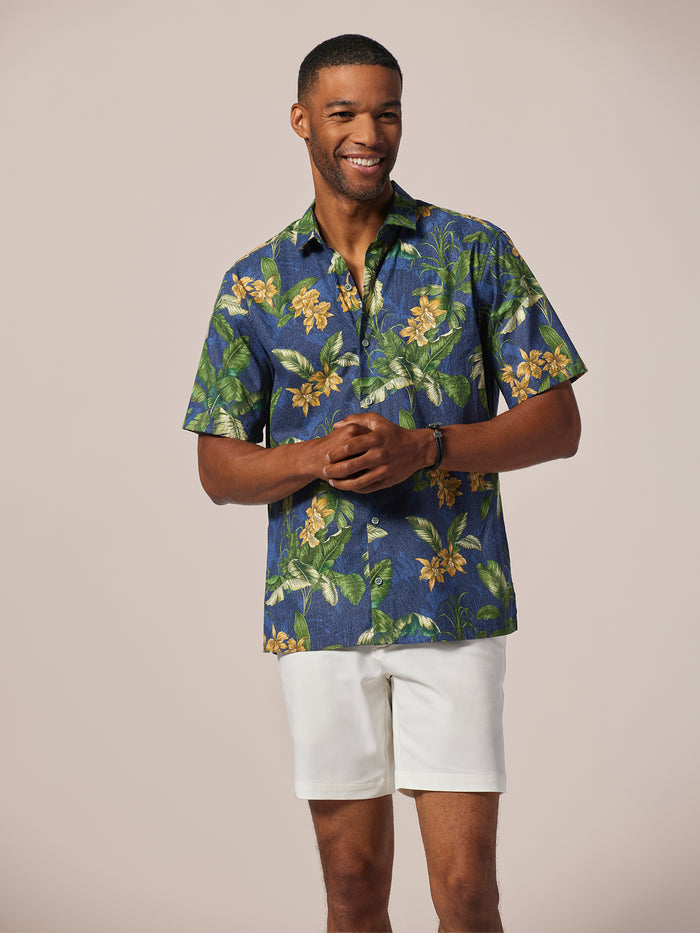 Blue orchid-print short-sleeve shirt with white shorts, front view, on plain backdrop.