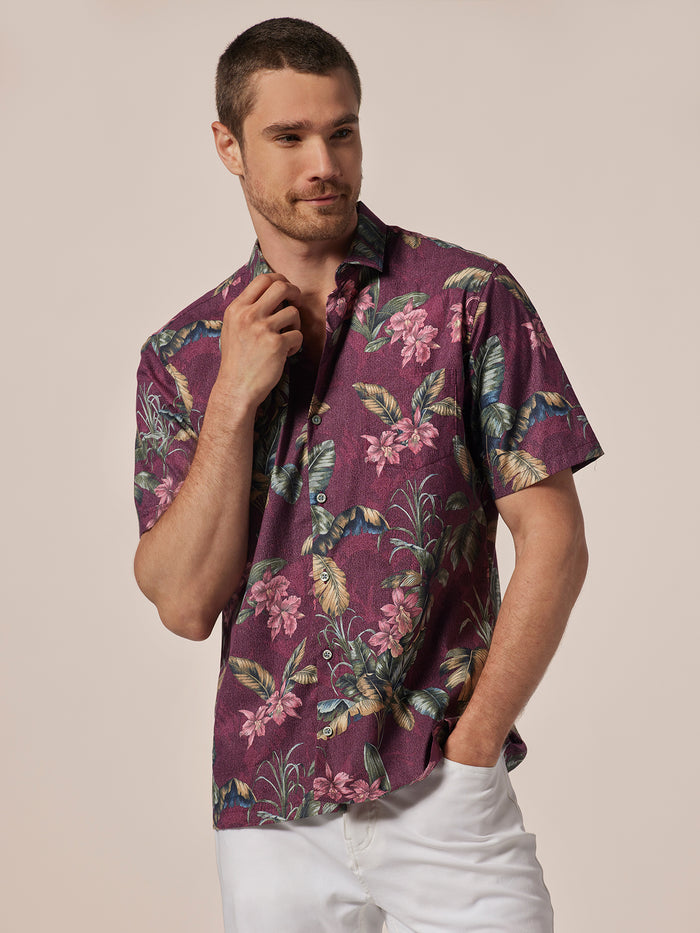 Maroon floral-print short-sleeve shirt and white pants, man standing with hand in pocket.