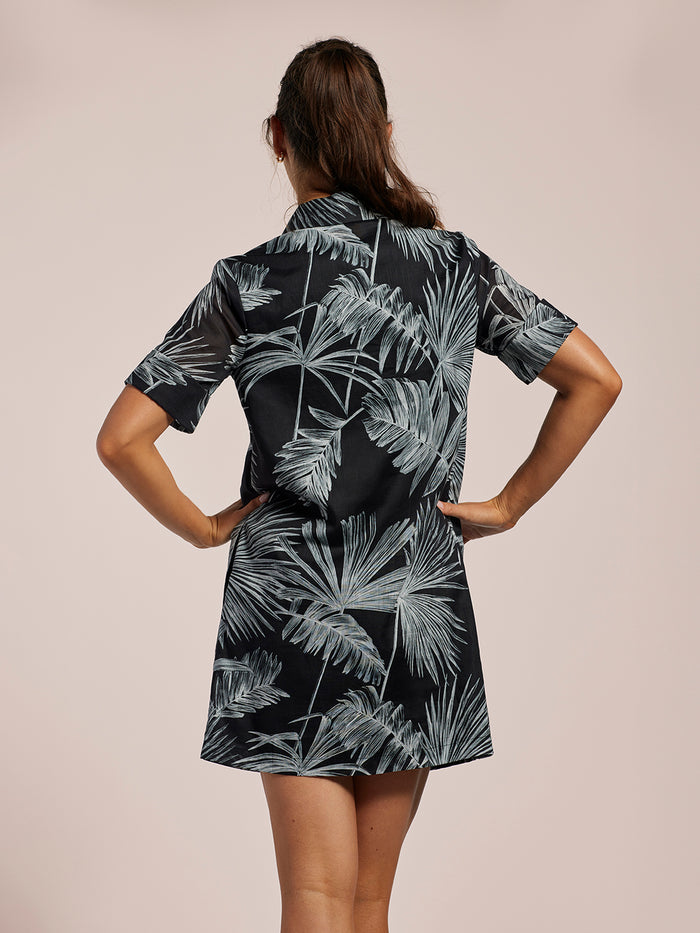 Black dress with white palm leaf print, back view with hands on hips.