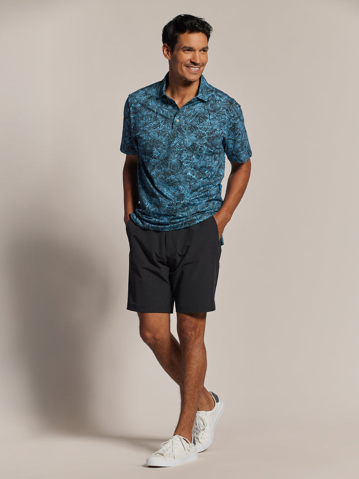 Blue hibiscus-print polo shirt with black shorts, front view, hands in pockets.
