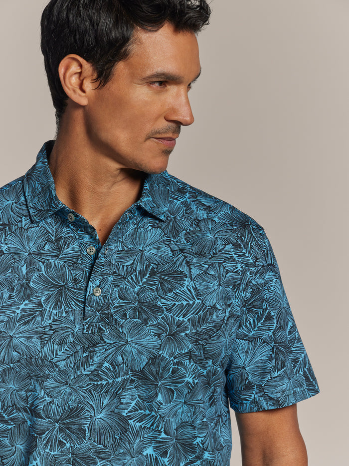 Blue hibiscus-print short-sleeve polo shirt, model looking left, beige background.