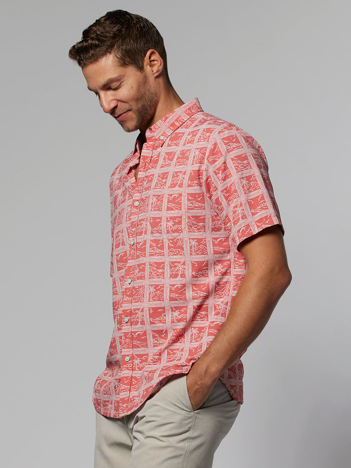 Red geometric short-sleeve shirt and beige pants. Man smiling with hands in pockets, front view.