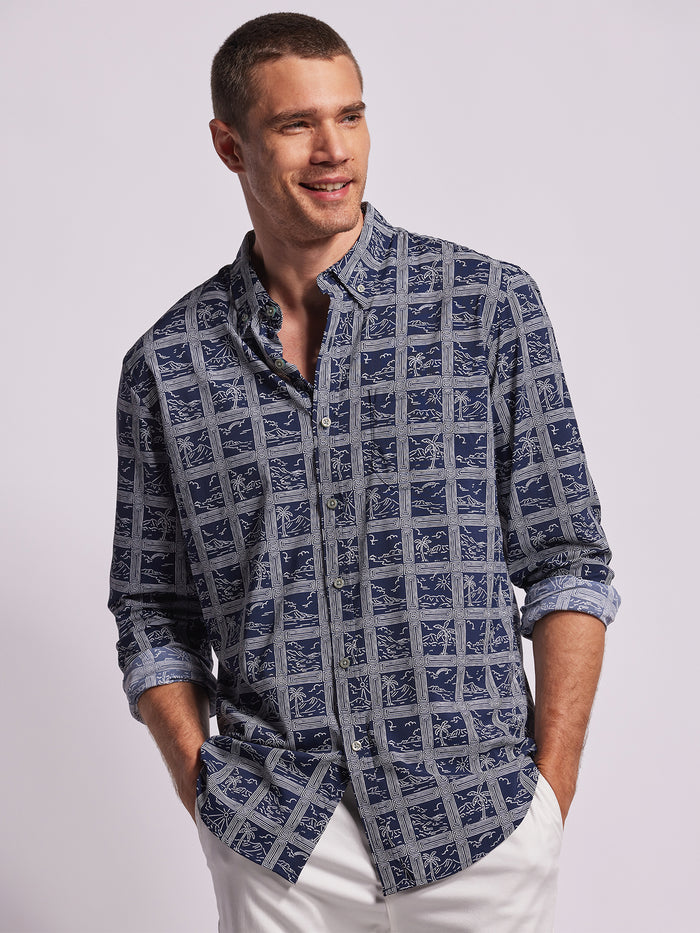 Blue and white grid-pattern long-sleeve shirt with geometric landscape print, sleeves rolled up, front view with white pants