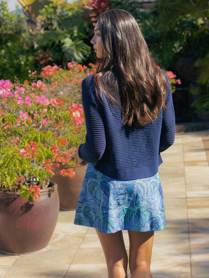 Navy knit cardigan and patterned skirt, woman standing front view outdoors among flowers in both images.