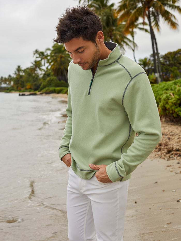 Light green stretch-cotton quarter-zip top with reversible light grey inside and white pants, full-length view on beach.
