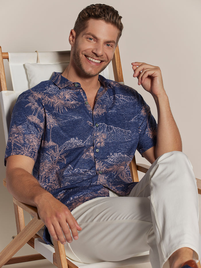 Light blue Coastal Engraving-print short-sleeve shirt and white pants, seated front view.