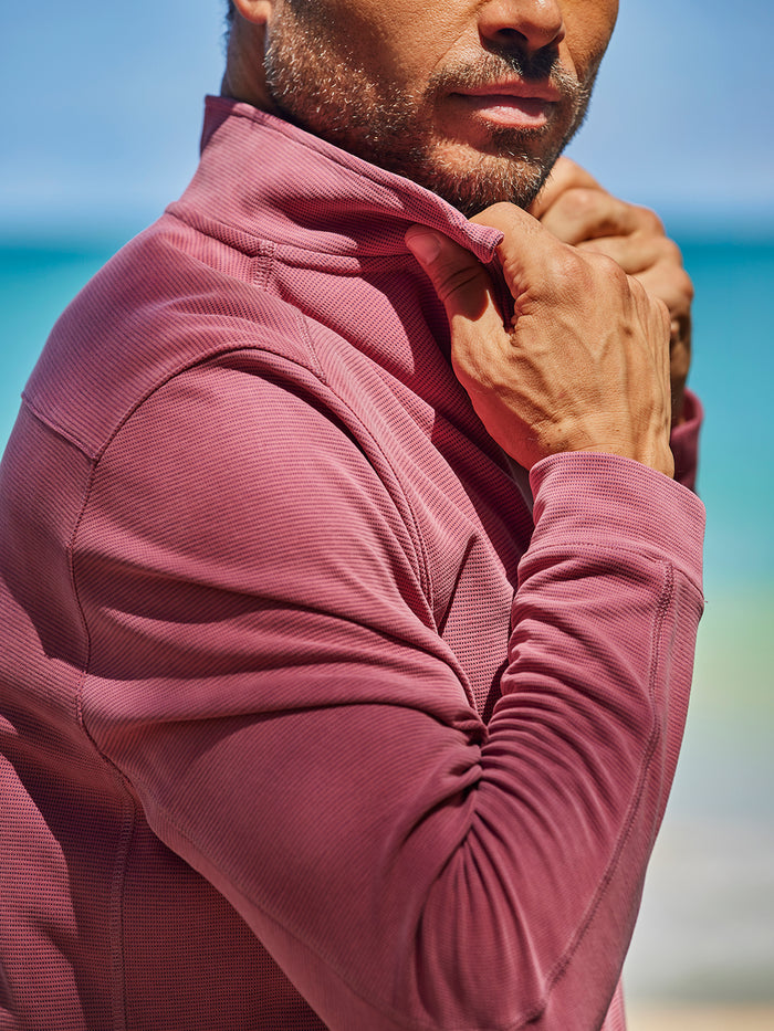 Light pink solid quarter-zip pullover model adjusting collar by the beach and ocean view.