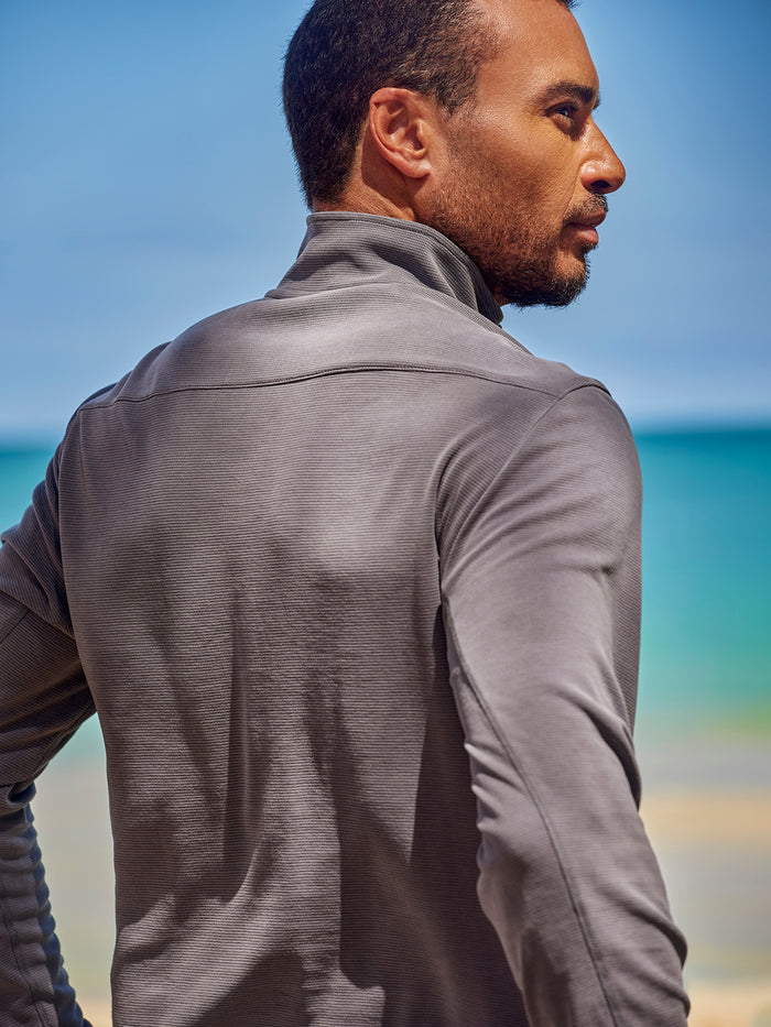 Gray solid long-sleeve quarter-zip pullover, side view, looking at the ocean under a clear sky in both images.