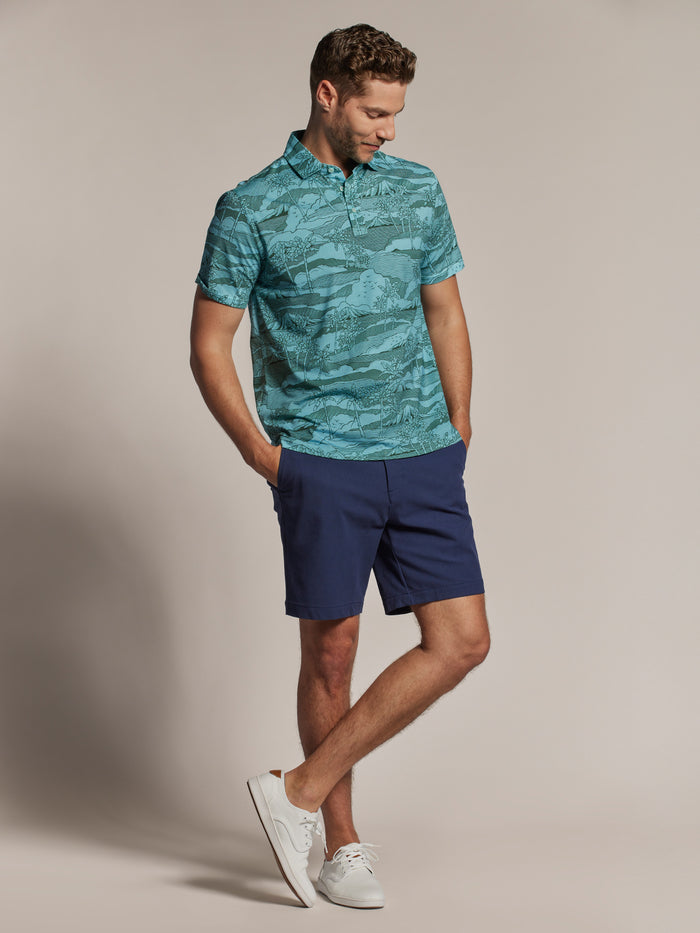 Light blue solid polo shirt and blue shorts with white sneakers, front view, hands in pockets.