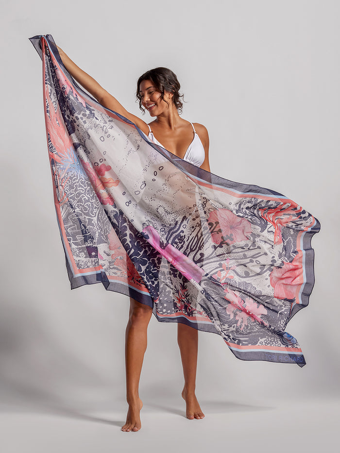 Coral floral-print pareo wrap, held by model in white bikini, front view.