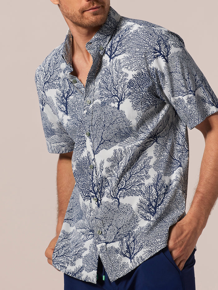 Blue and white and blue coral patterned short-sleeve shirt, man standing with hands in pockets, front view.