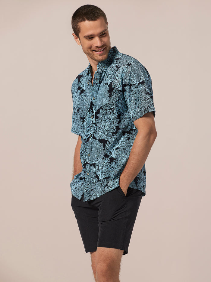 Coral short-sleeve shirt and black shorts, front view, hands in pockets.