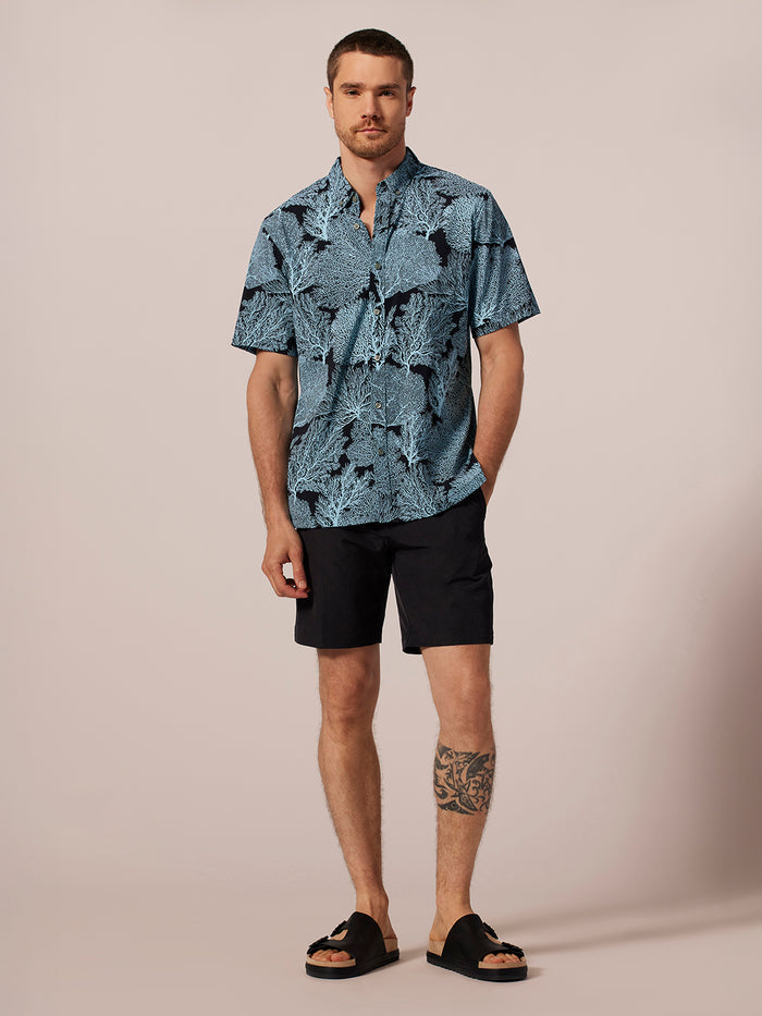 Coral short-sleeve Tradewind Technology® shirt, front view with black shorts and sandals.