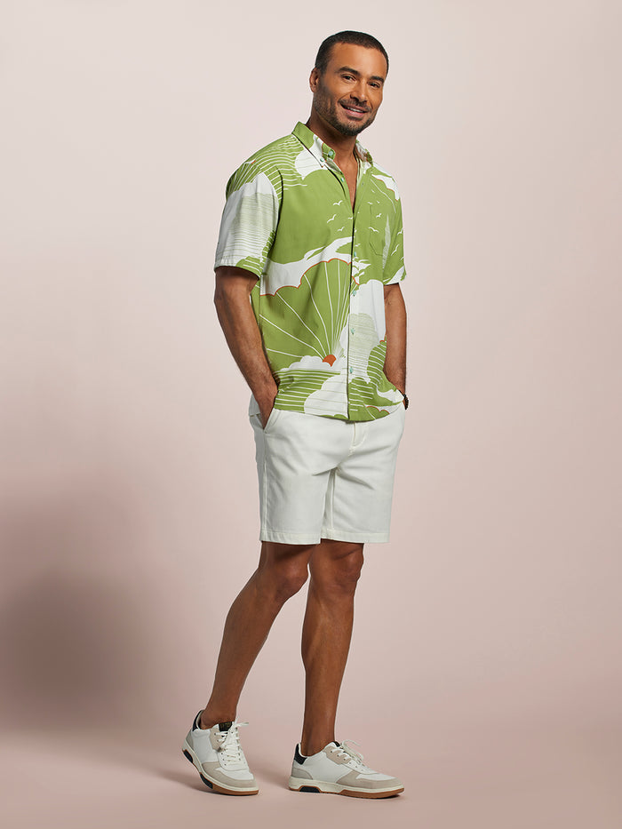 Green patterned short-sleeve shirt and white shorts, front view, hands in pockets.