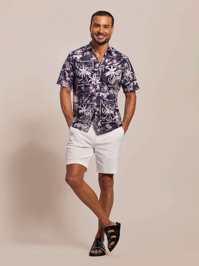 Black and white pinkish palm-print short-sleeve cotton shirt, front view of a man with white shorts and black sandals.