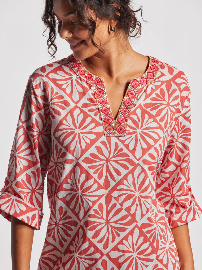Pink and white patterned caftan with embroidered neckline, woman looking down left.