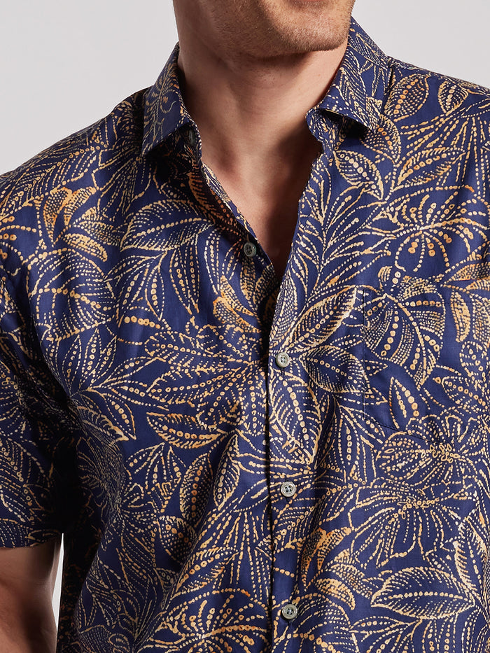 Navy blue Hawaiian-made shirt with gold and white leaf print, open collar, front view .
