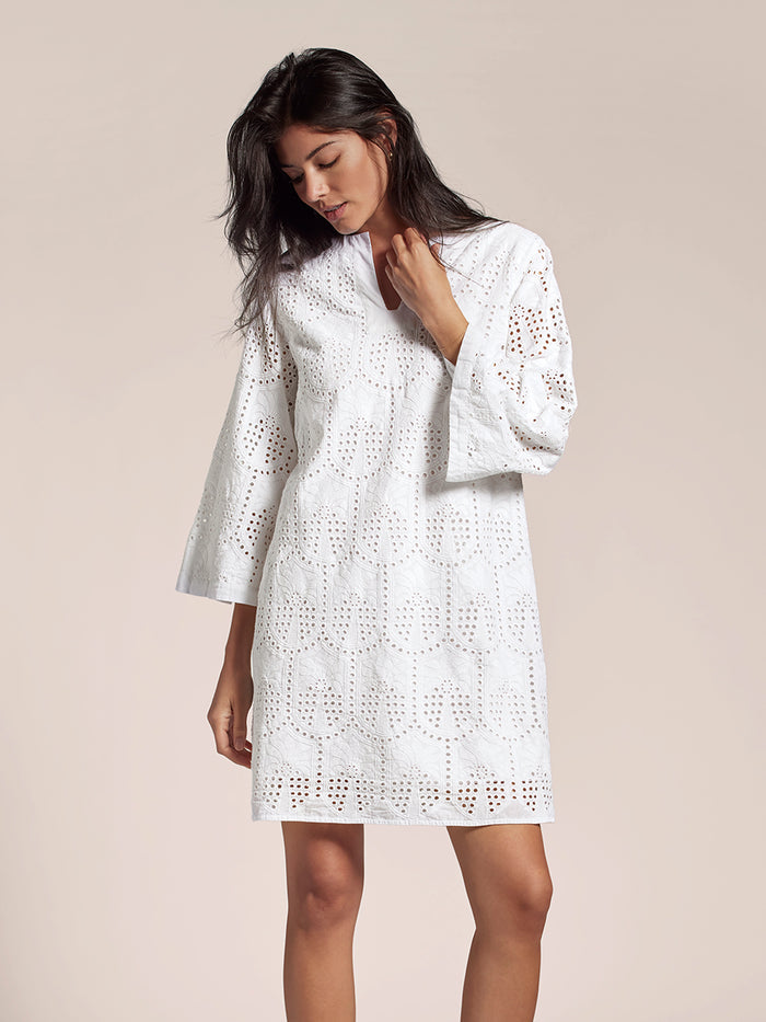 White eyelet palm-pattern midi dress, woman looking down with hand near collar.