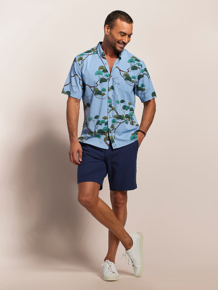 Light blue, short-sleeve shirt with Japanese pine and green foliage print, front view against light background.