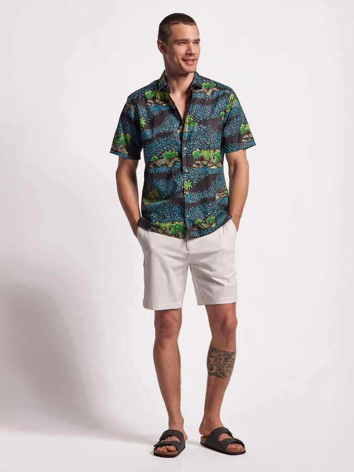 Blue and white graphic print short-sleeve shirt, front view with white shorts and sandals.