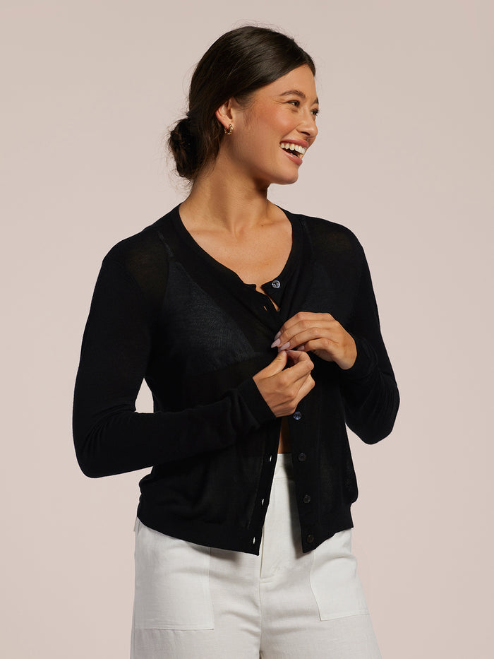Black open-front knit cardigan over white pants, front view.