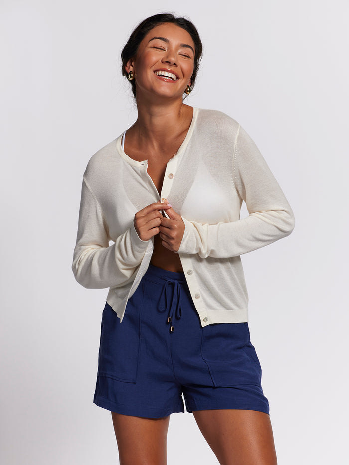 Cream cardigan, long sleeves, over white top and blue shorts, front view.