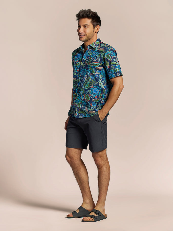 Navy cotton short-sleeve shirt with blue, green, and red tropical leaves prints, a man standing, with dark shorts and sandals.