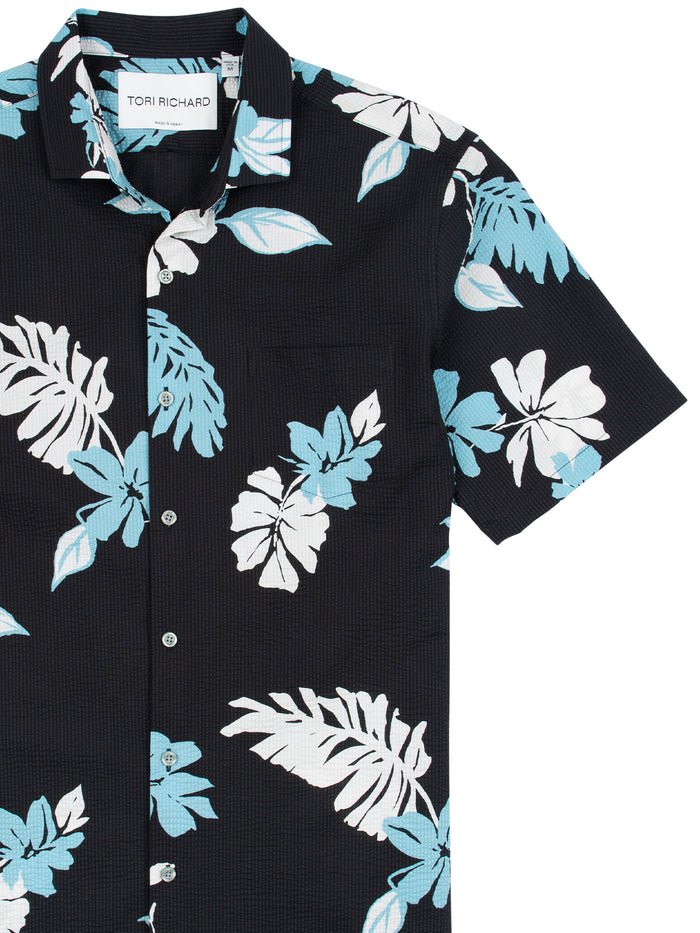 Black short-sleeve shirt with blue and white tropical leaf print, front view, white buttons.