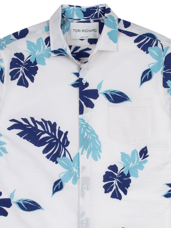 White cotton shirt with blue/teal tropical leaf print, collared, chest pocket, front view.
