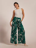 White sleeveless top, green frond-print pants, and beige heels; full body front view.