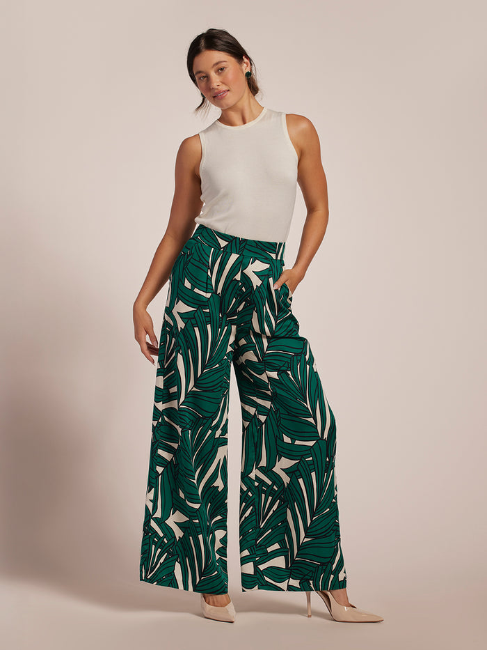 White sleeveless top, green frond-print pants, and beige heels; full body front view.