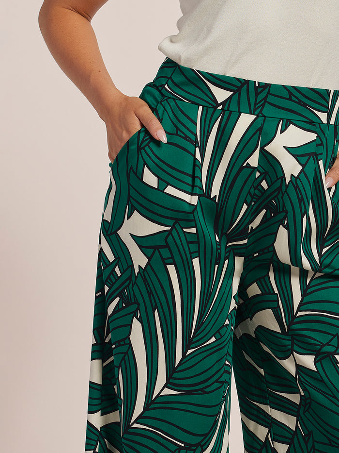 Green and white leaf-print wide-leg pants, side view with hand in pocket.