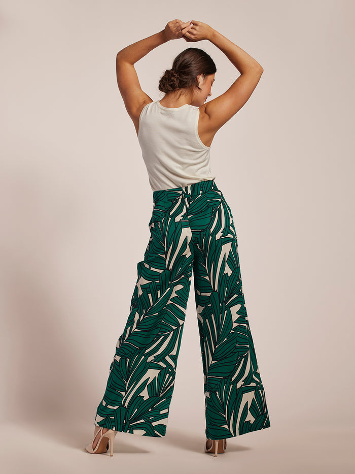 White tank top and green frond-print pants, back view with arms raised.