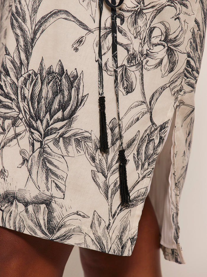 Cream skirt with black floral sketch print, tassel cords, and side slit, close-up view.