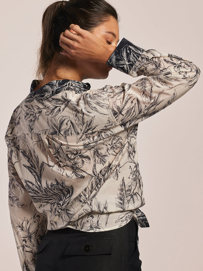 White floral-print cotton voile oversized blouse, back view, with black pants and hand on neck