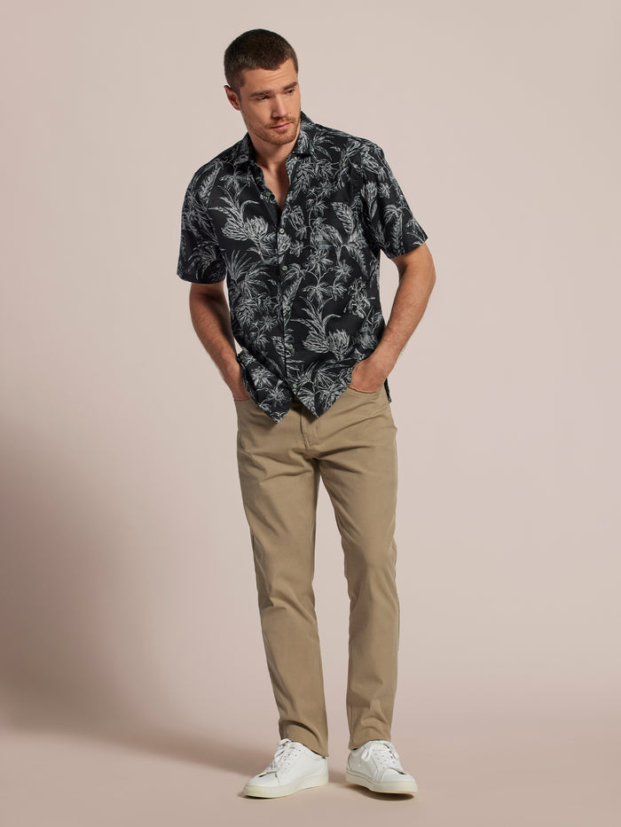 Black floral-print short-sleeve Hawaiian shirt, khaki pants, front view, hands in pockets.