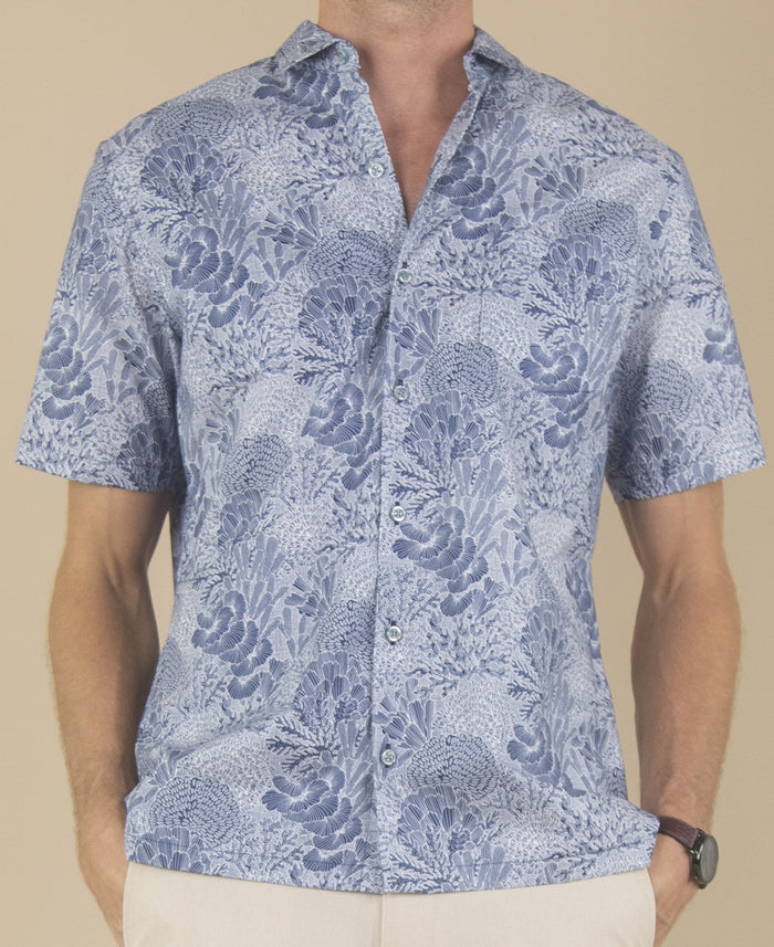 Blue graphic-print short-sleeve shirt and light pants, front view on beige background.